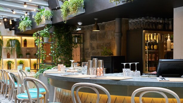 Zona de bar con mostrador, taburetes y una variedad de copas.