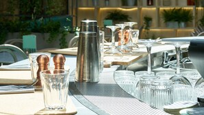 Un área de comedor al aire libre con mesas dispuestas para dos, con candelabros metálicos, vasos transparentes y saleros y pimenteros de cobre.