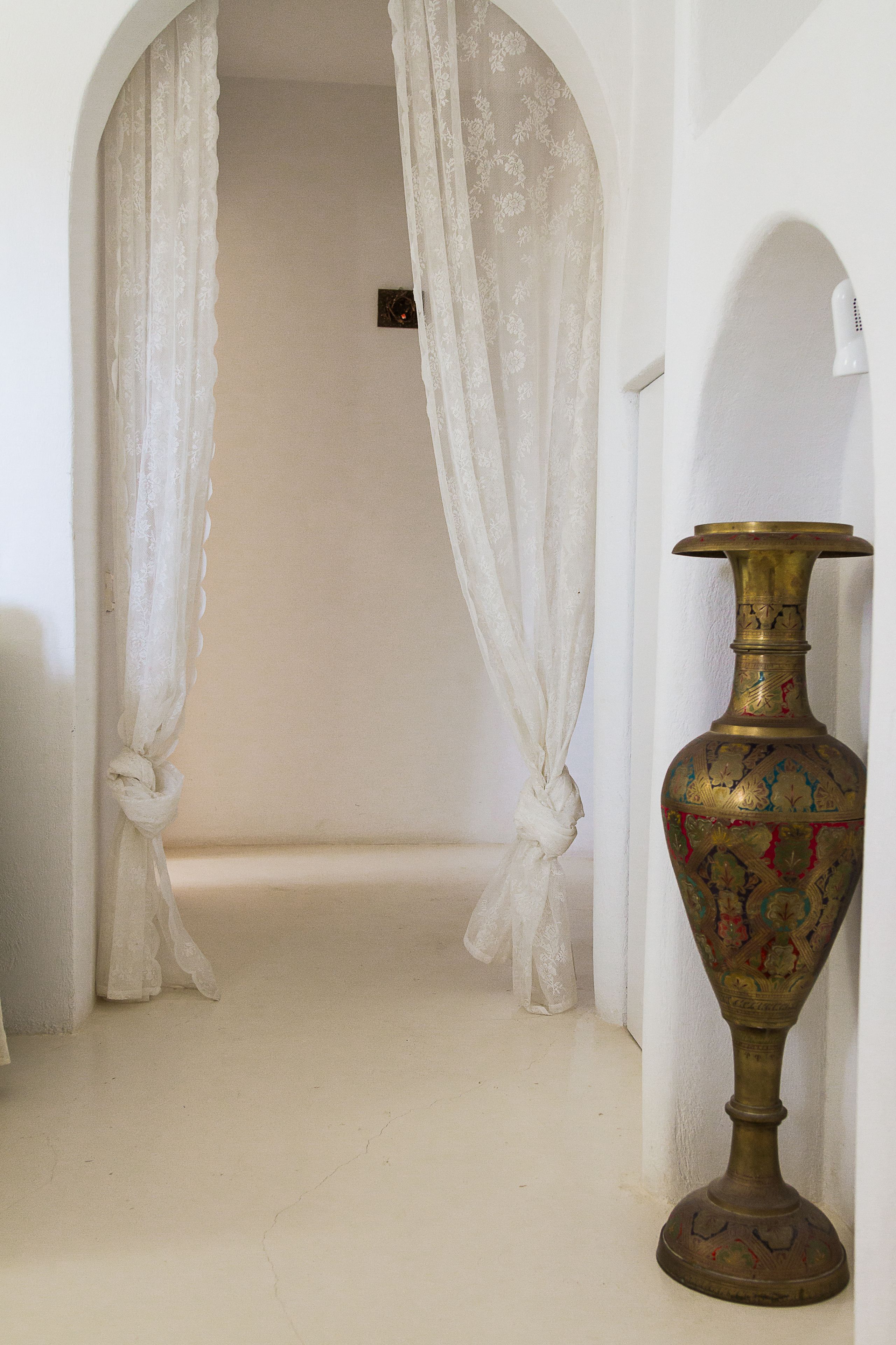 A hallway with a white floor, a decorative vase, and sheer curtains.