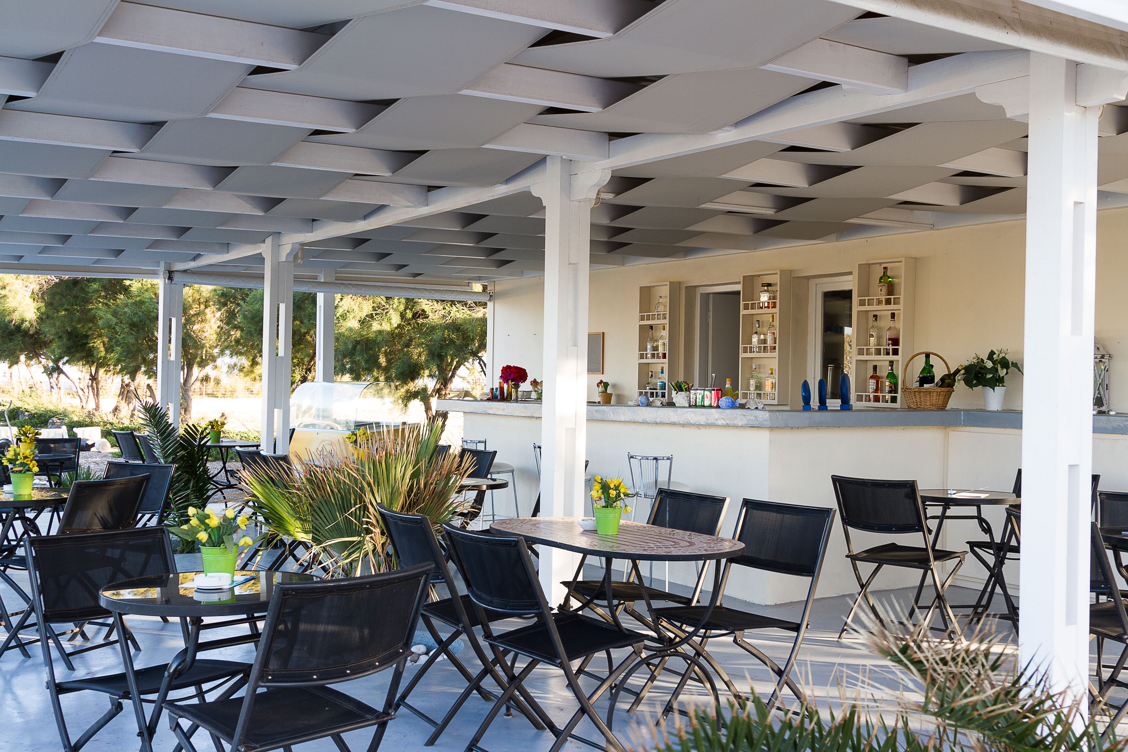 An outdoor patio with tables and chairs, a bar area, and a view of trees.