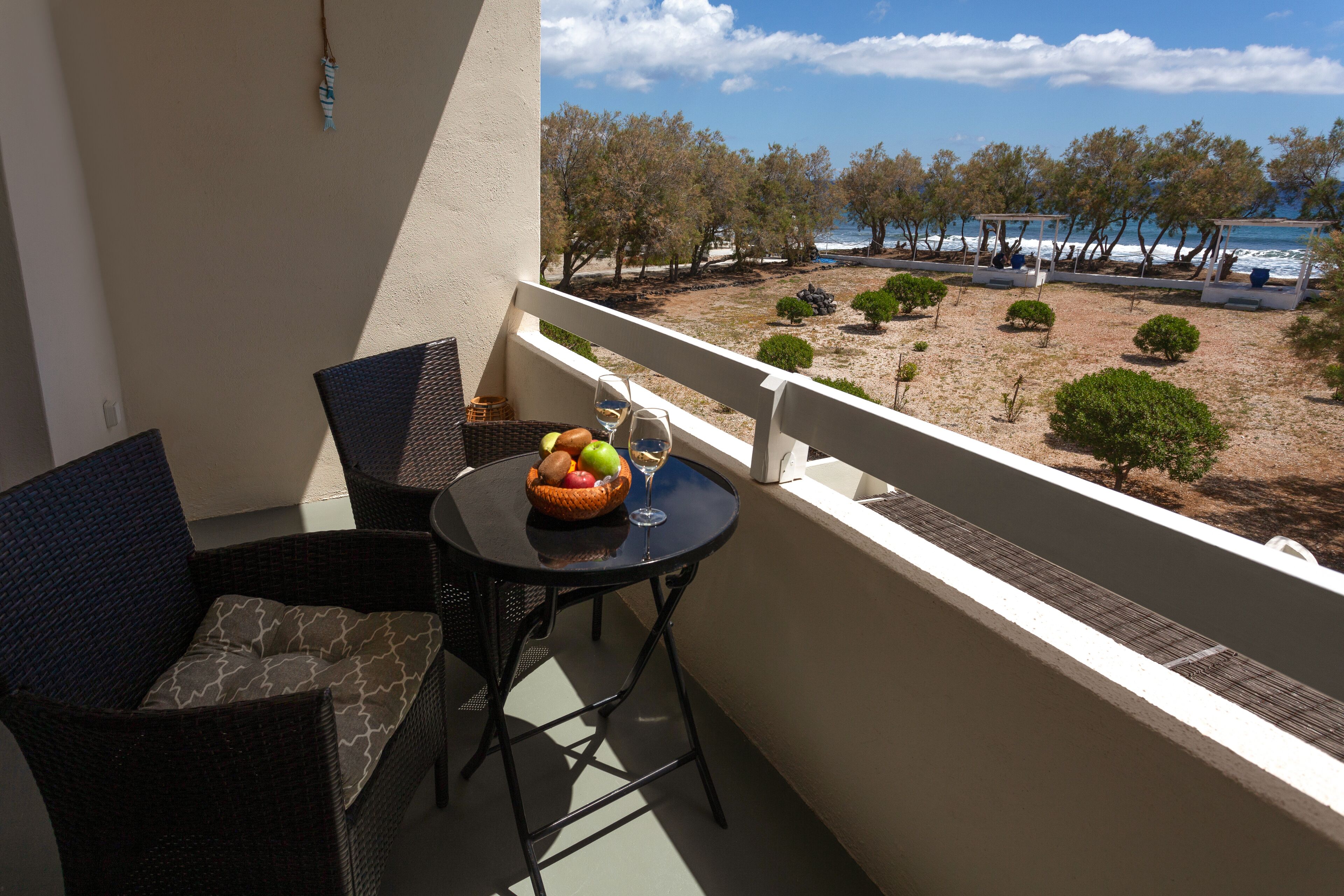 A balcony with wicker furniture, a table with fruit and a glass, and a view of the beach and sea.
