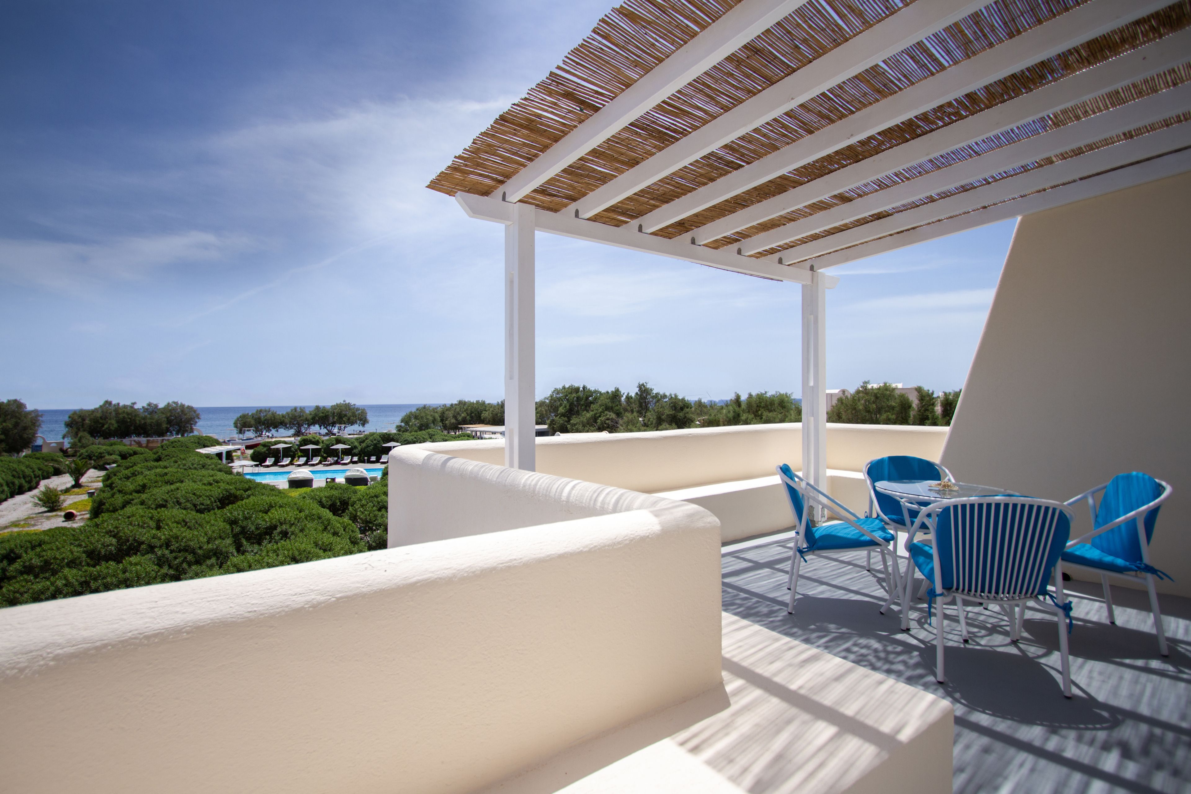 A terrace with a view of the sea, white walls, and blue chairs.