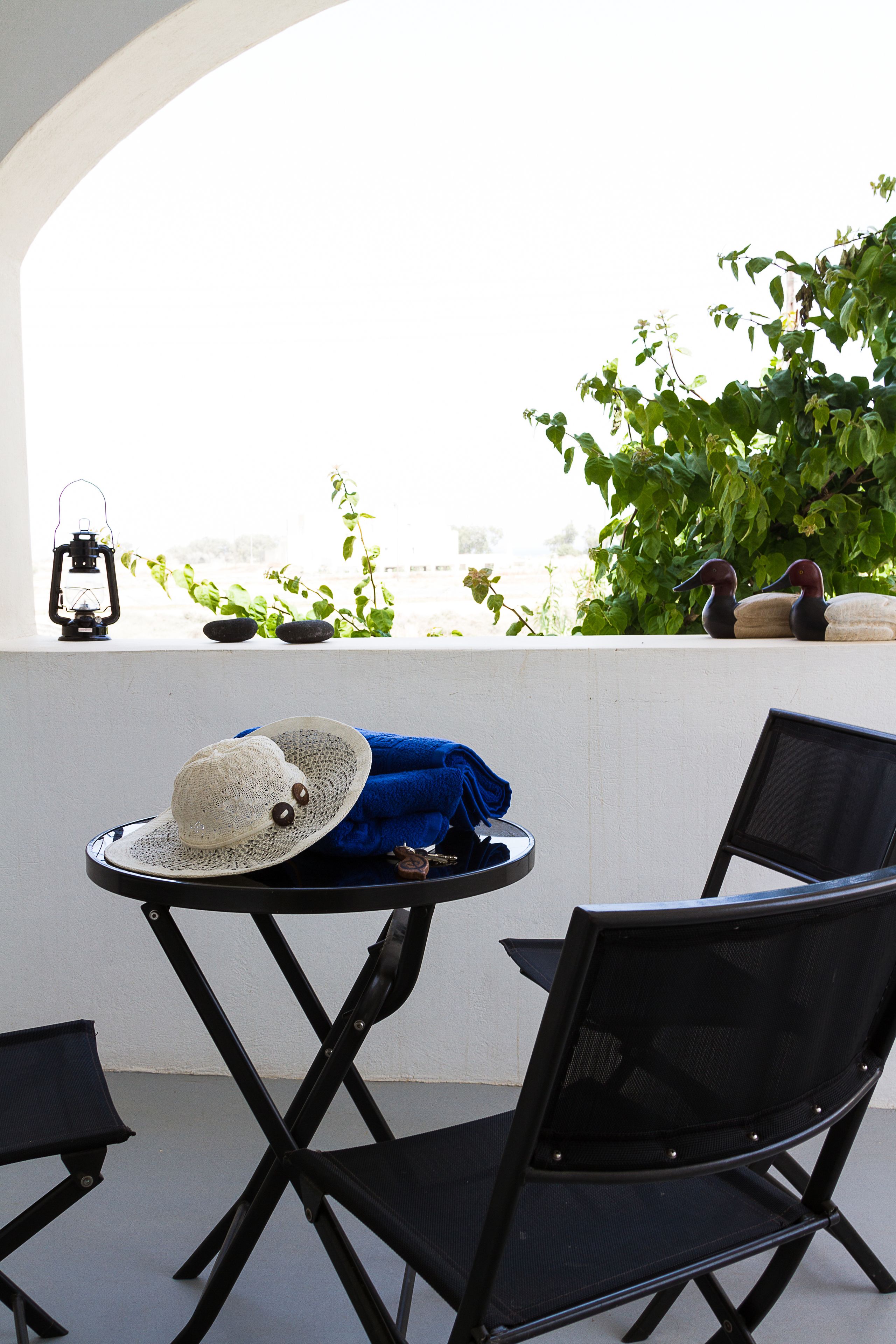 A balcony with a table, two chairs, a hat, a lantern, and decorative stones.