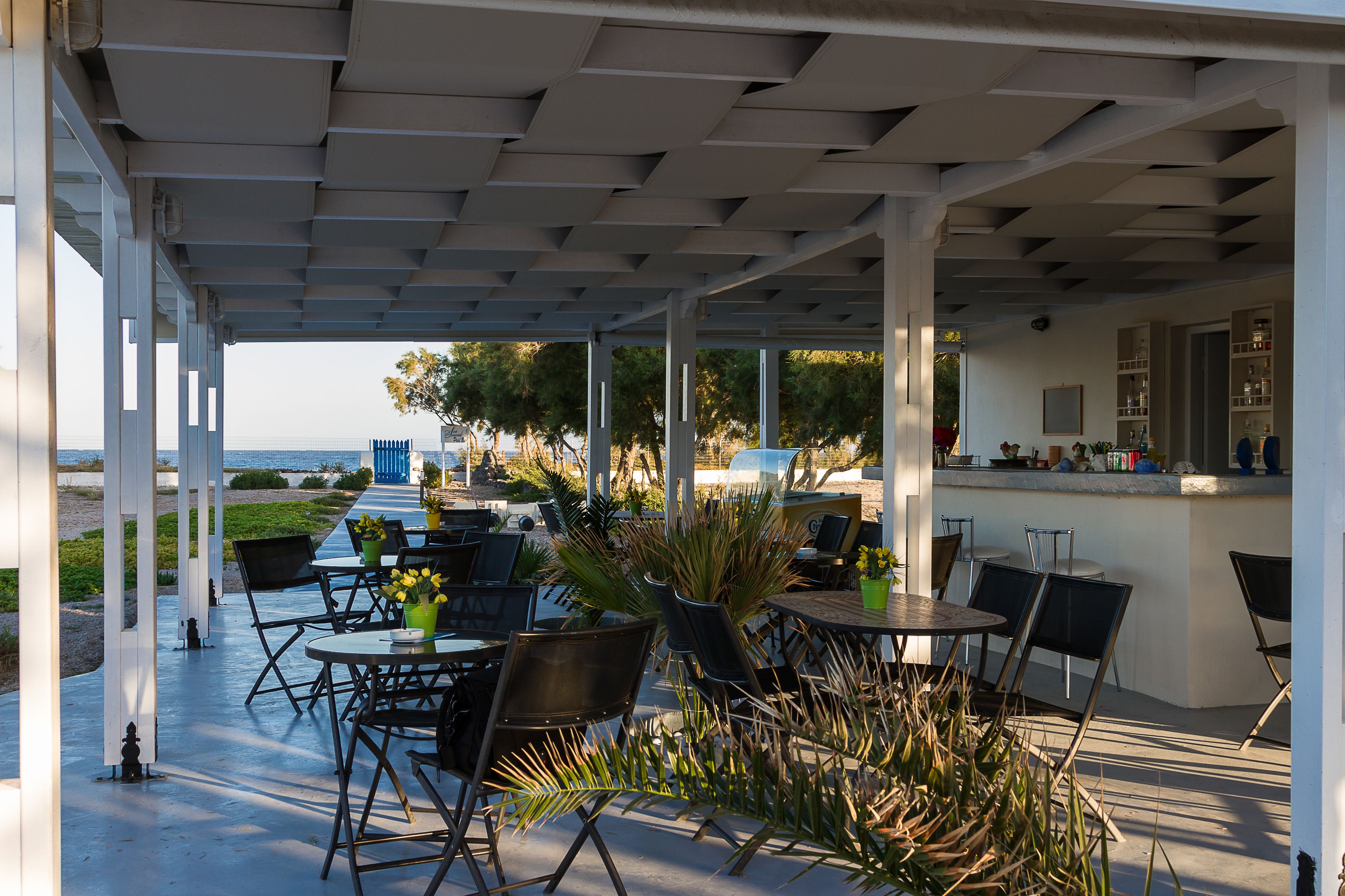 An outdoor patio with tables and chairs, a bar area, and a view of the sea.