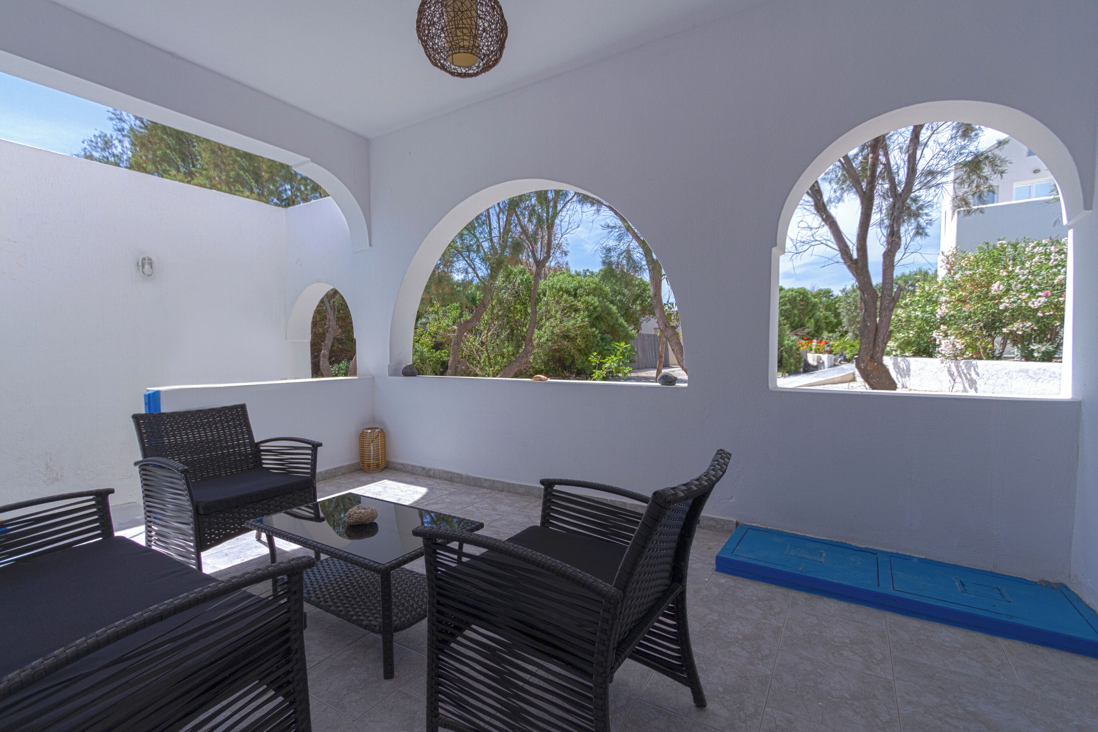 A patio area with wicker furniture, a table, and a view of trees and a building through arched windows.