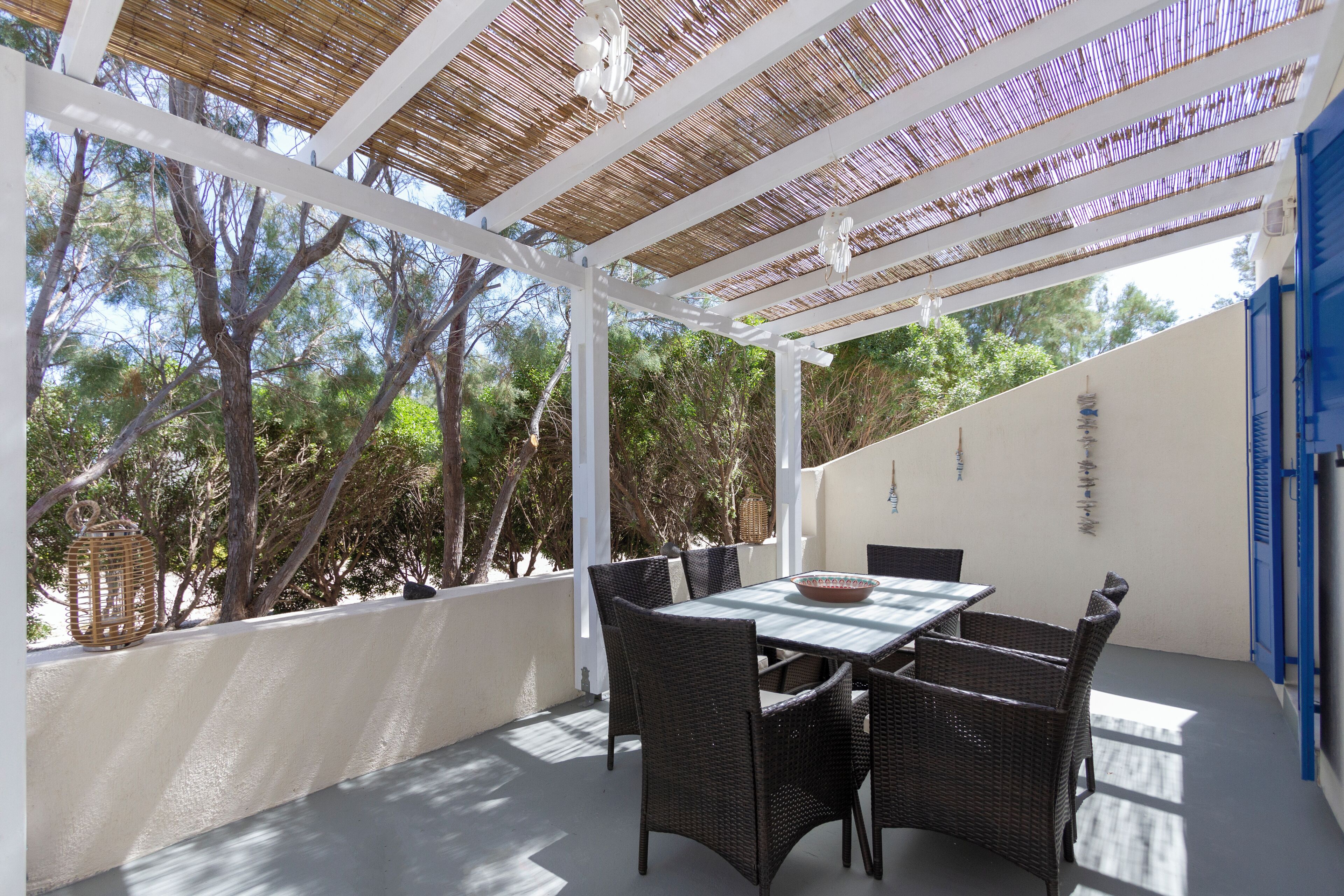 A covered patio with a table and chairs, surrounded by trees.