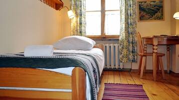 Ein Schlafzimmer mit einem hölzernen Bett, einem Schreibtisch, einem Stuhl, einem Heizkörper und einem Fenster mit Vorhängen.