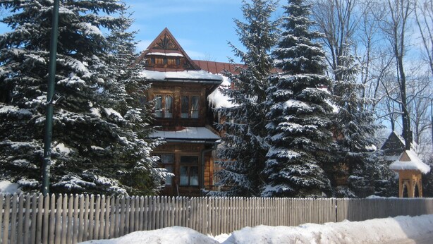 A large wooden house with a steep roof, surrounded by snow-covered trees and a wooden fence. - Willa Orla (Zakopane)