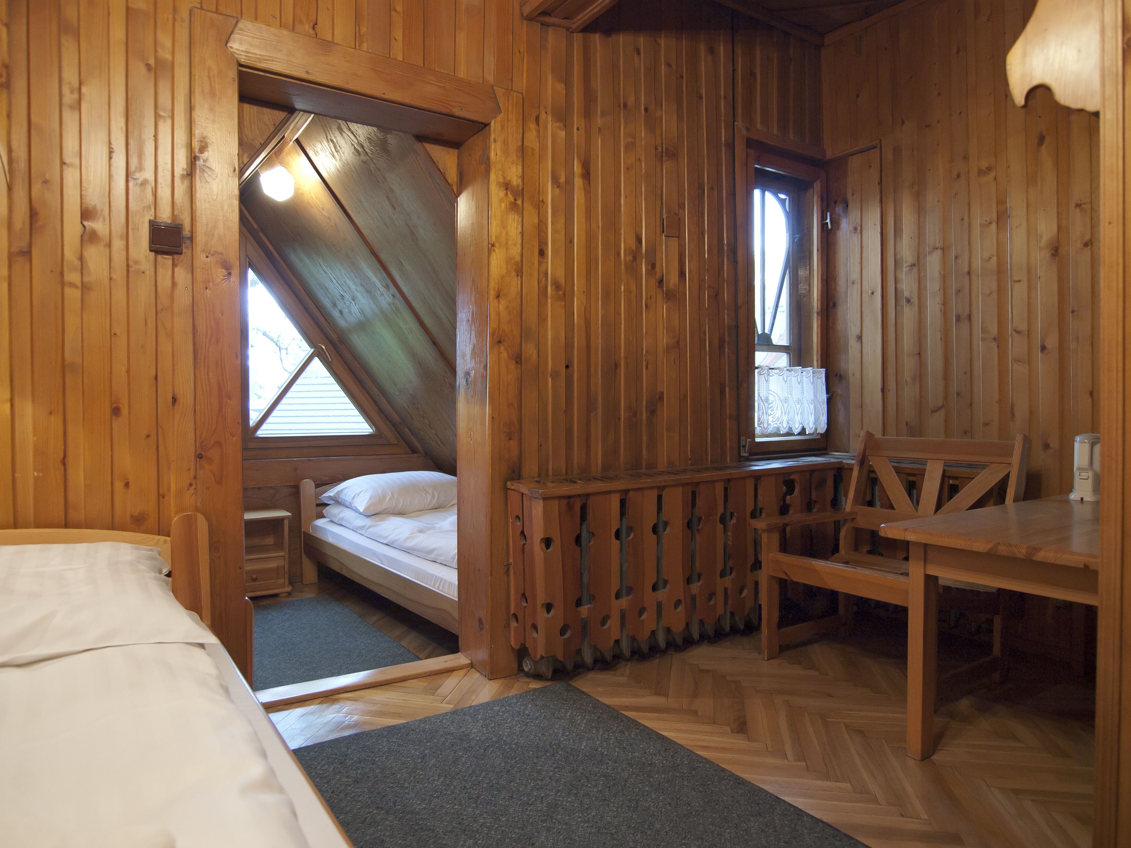 Una habitación tipo cabaña de madera con una cama, una mesita y una ventana.