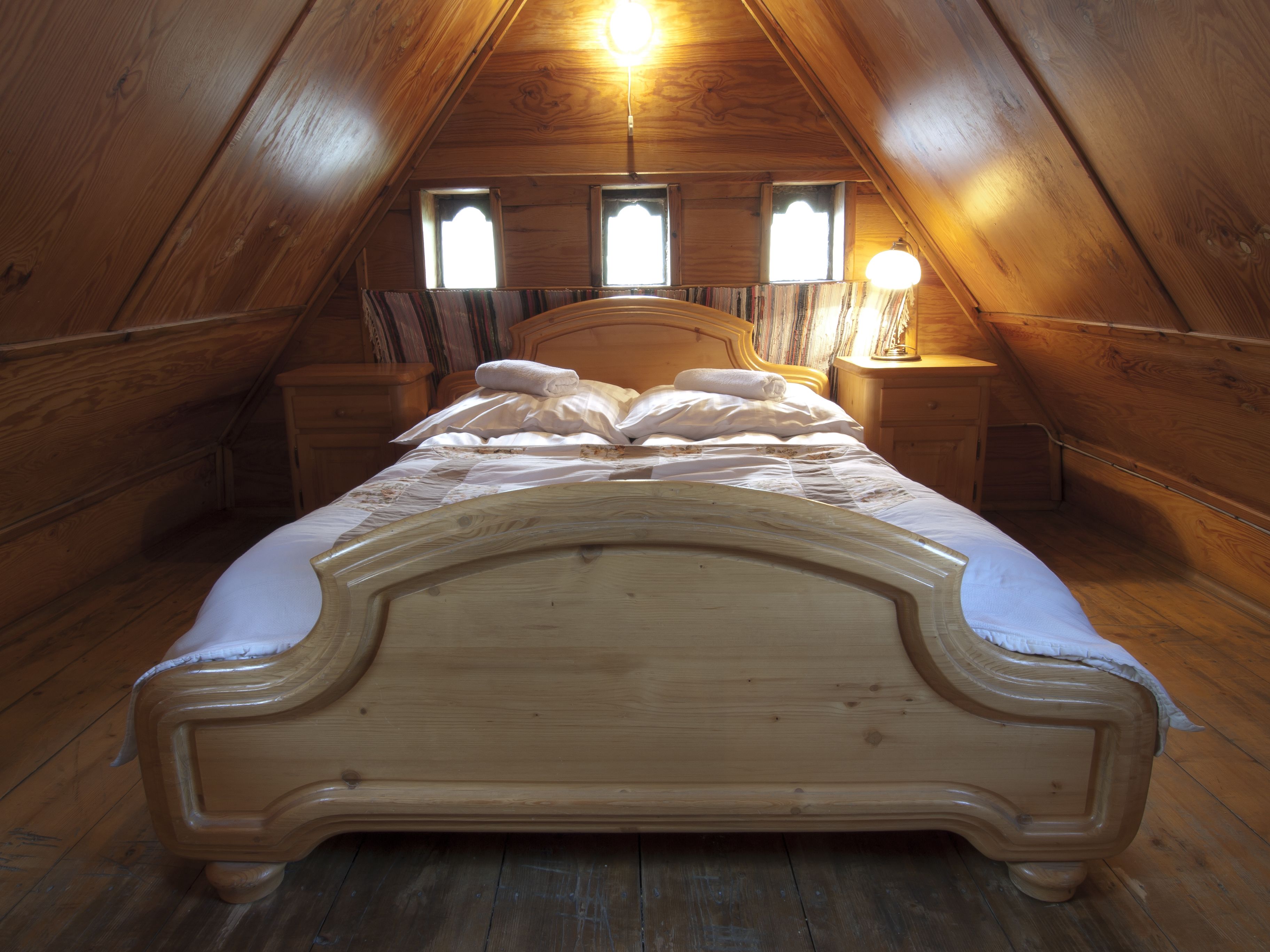 A wooden bed in a sloped ceiling room with two bedside lamps and a window.