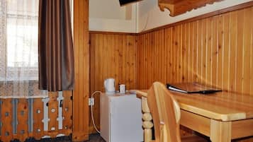 A corner room with wooden paneling, a small white refrigerator, a wooden table, and a TV mounted on the wall.