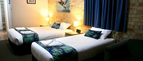 Une chambre d’hôtel avec deux lits, chacun équipé d’un oreiller et d’une couverture, une table de chevet avec une lampe et un tableau accroché au mur.