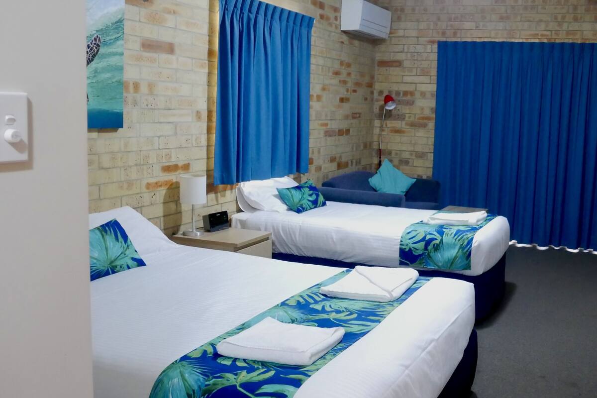 A hotel room with two beds, a brick wall, and blue curtains.