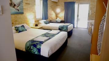 A hotel room with two beds, a small table, a chair, a window with curtains, and a wall-mounted air conditioner.