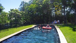 A swimming pool with a clear blue water surface, surrounded by a black metal fence and lush green grass. - Emeraldene Inn & Eco-Lodge (Urraween)