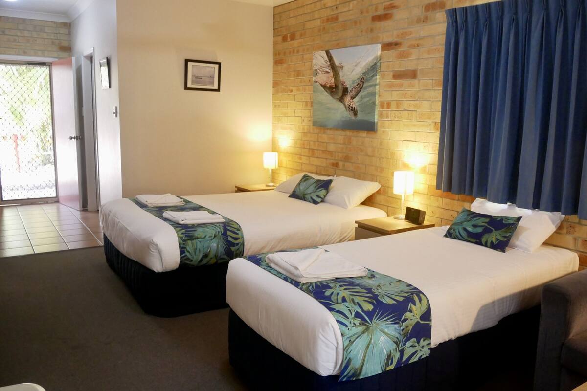 A hotel room with two beds, a brick wall, a painting of a sea turtle, and a view of the outside.