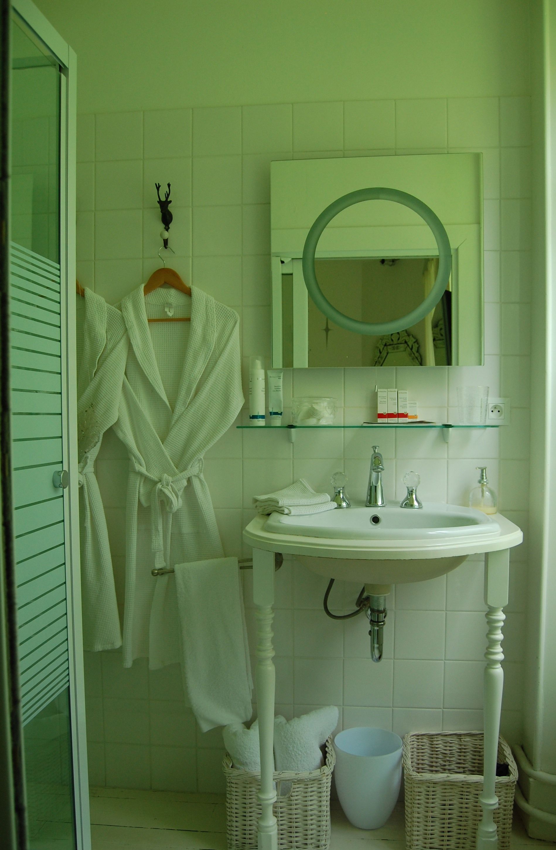 A bathroom with a white sink, a mirror, a robe hanging on the wall, and wicker baskets.