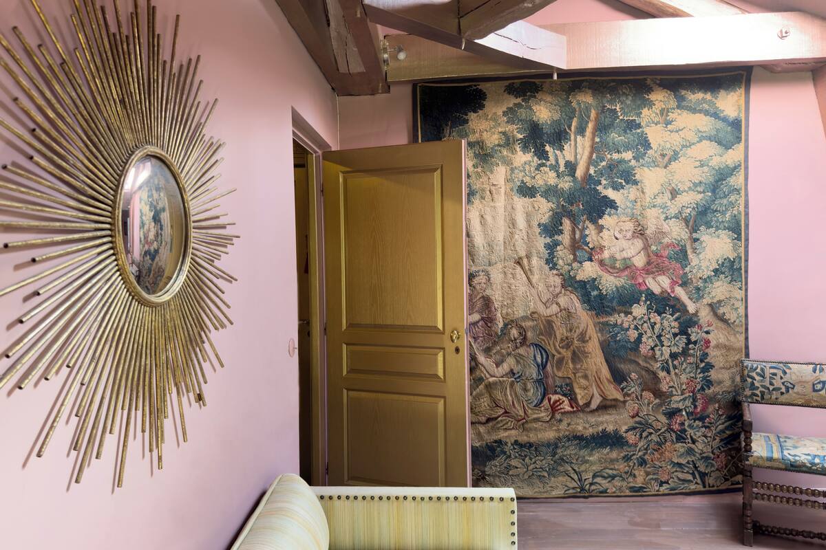 A room with a sunburst mirror, a door, and a tapestry with a forest scene.