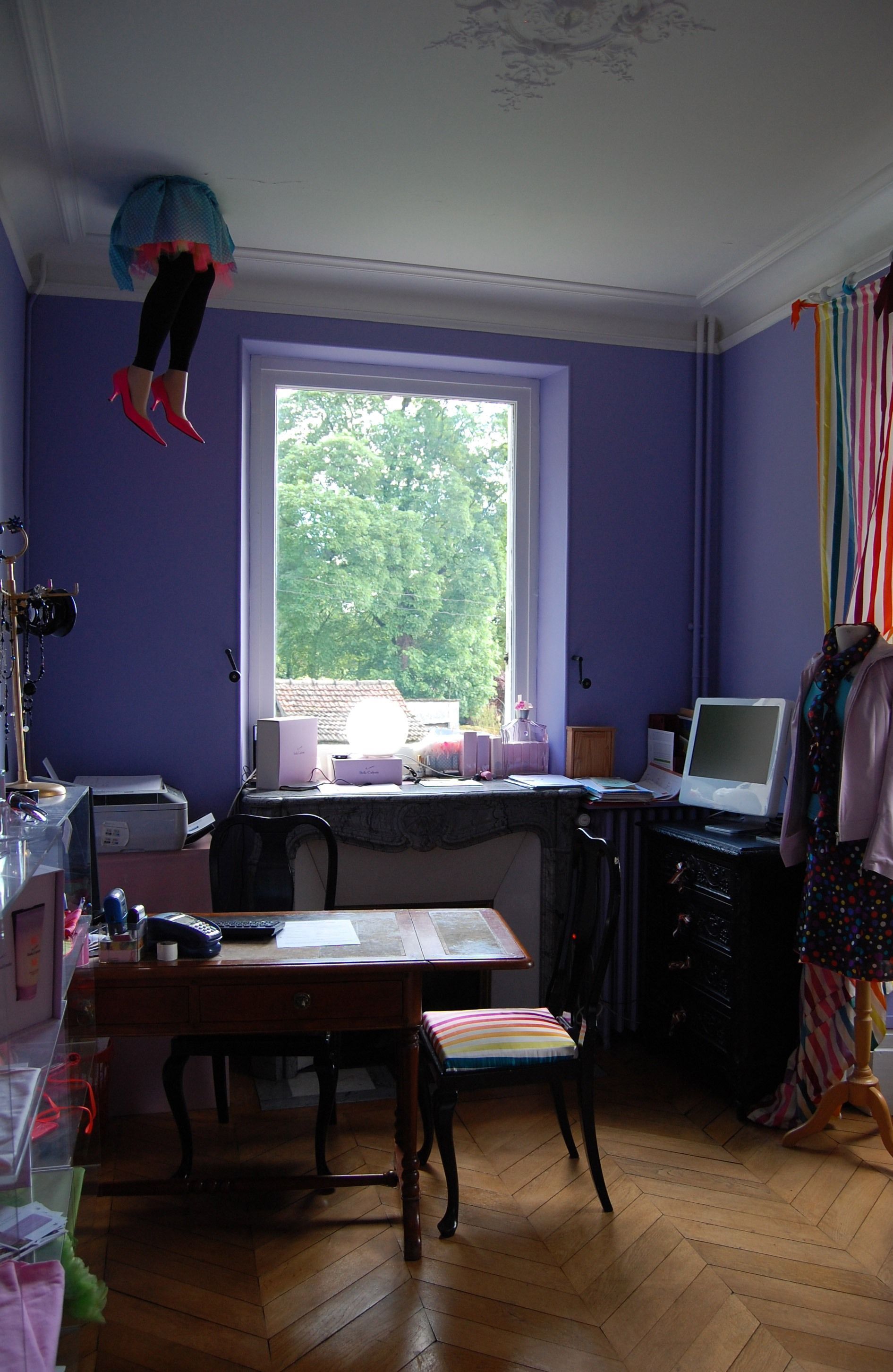 A room with a large window, a desk with a computer, a chair, and a mannequin.