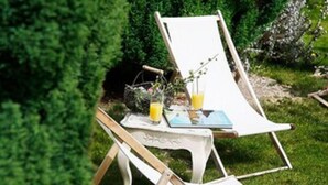 Dos sillones blancos con una mesa entre ellos, ubicados en un área verde con una mesa pequeña y una cesta de flores.