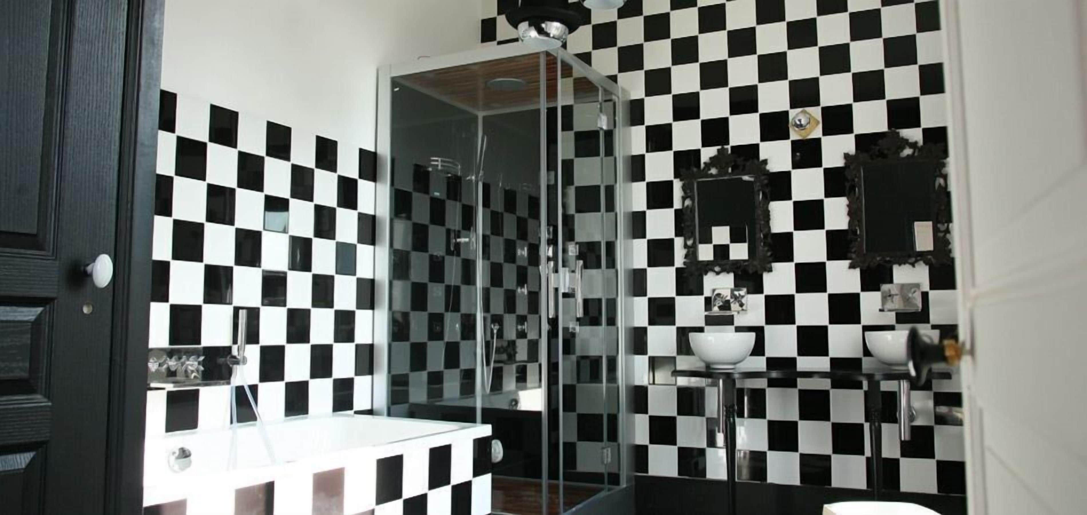 A bathroom with a black and white checkered tile backsplash, a glass shower enclosure, and a white sink with a mirror above it.
