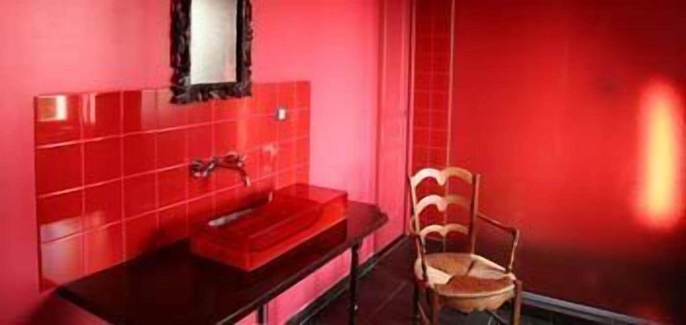 A bathroom with a red tiled wall, a black sink, and a wooden chair.