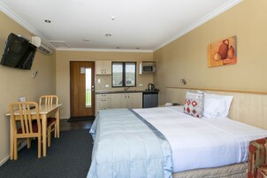 Habitación de hotel con cama, escritorio, silla, microondas, lavamanos y televisión.