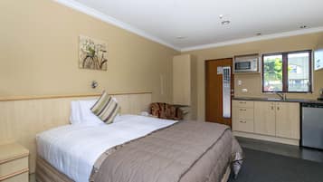 A hotel room with a bed, a small desk, a microwave, a sink, and a window.