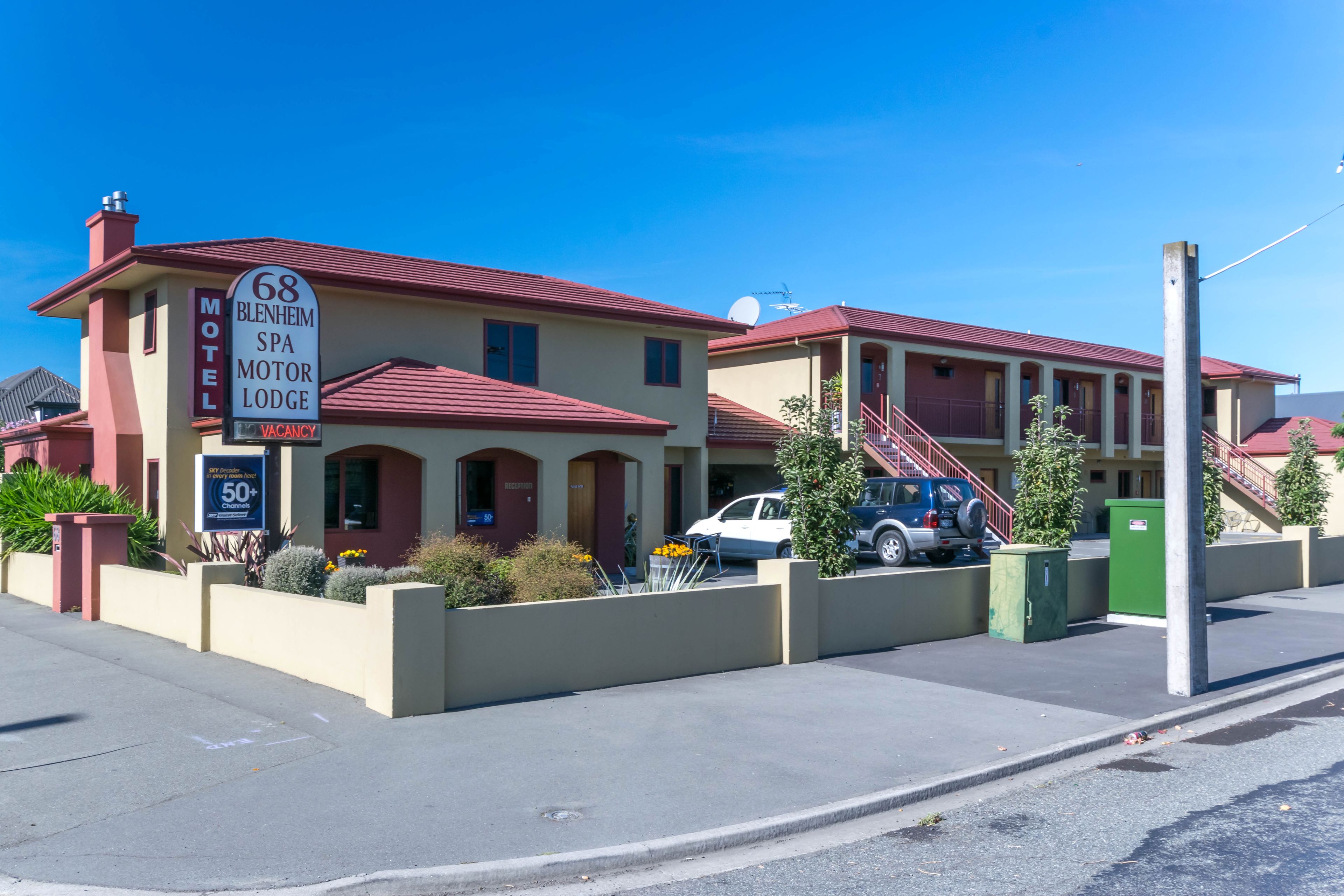 Un motel con techo rojo y paredes color crema, mostrando un cartel que indica disponibilidad.