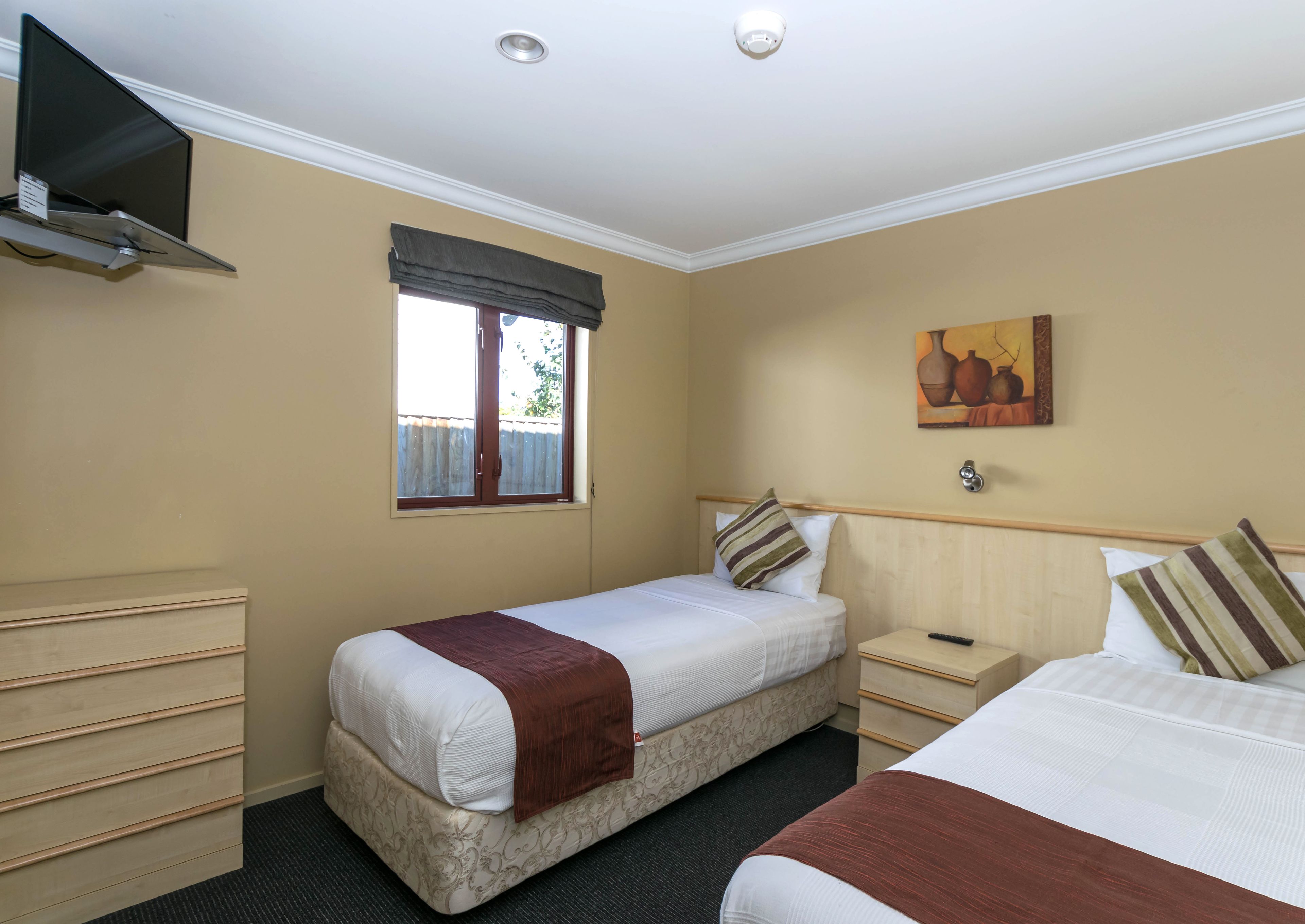 A hotel room with two beds, a TV mounted on the wall, a window with a view, and a painting on the wall.