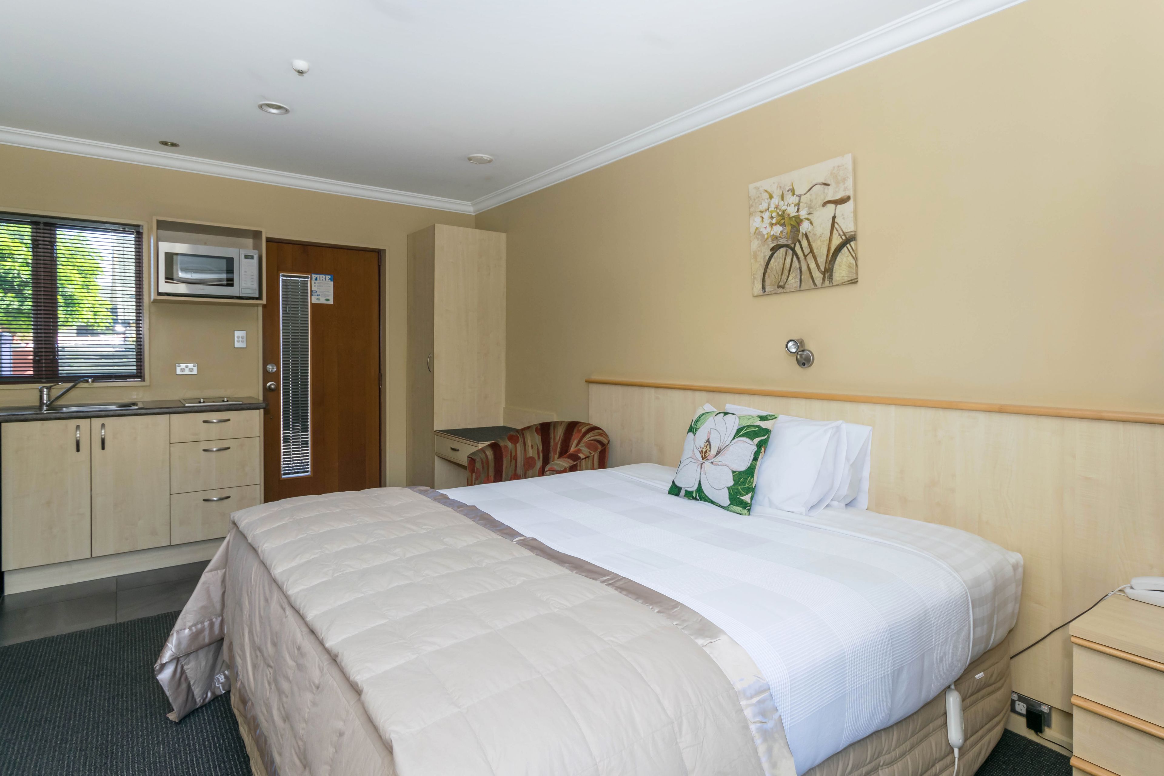 Quarto de hotel com cama, escrivaninha, micro-ondas, janela e porta.