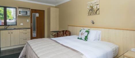 Quarto de hotel com cama, escrivaninha, micro-ondas, janela e porta.