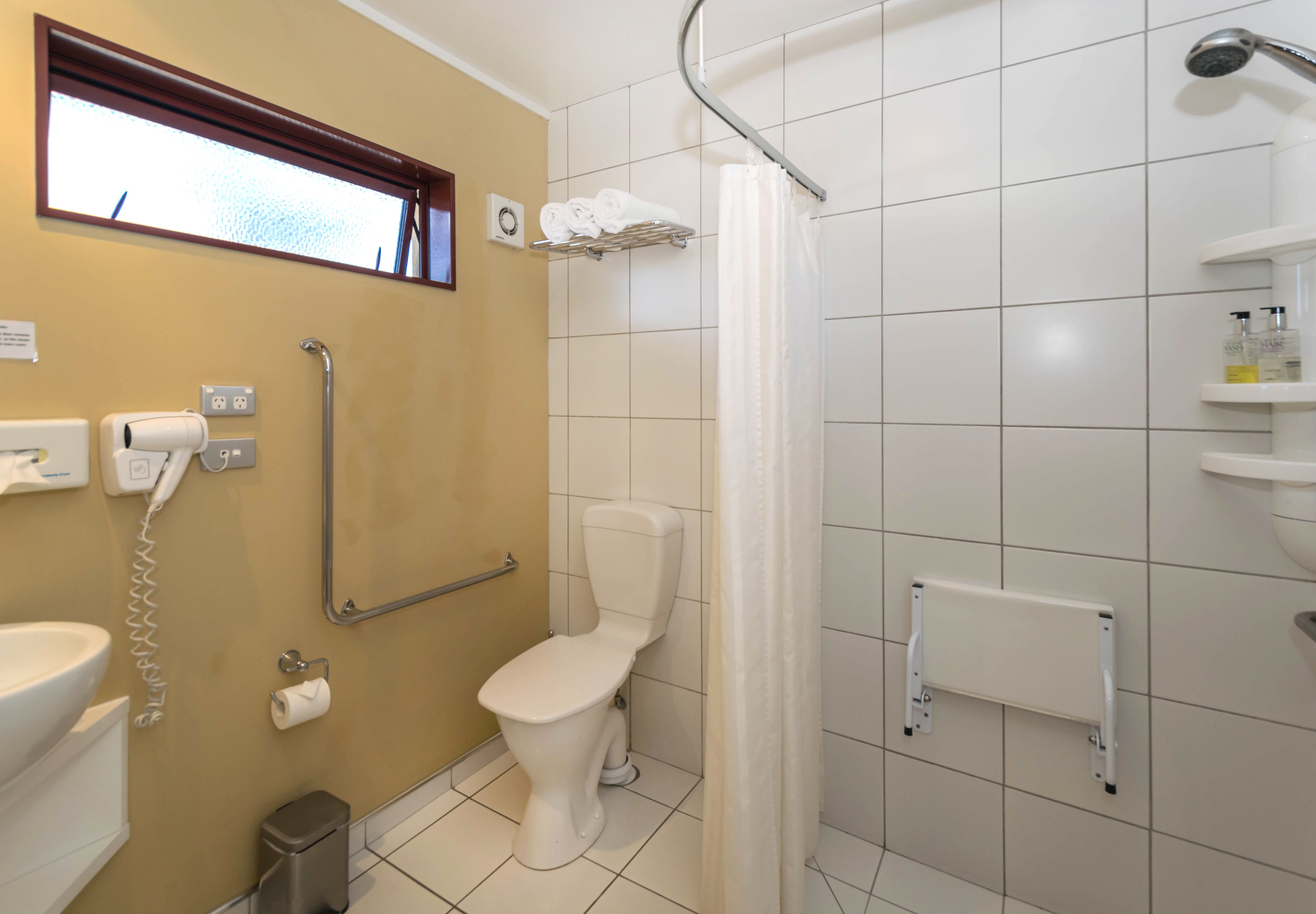 A bathroom with a toilet, hand dryer, and a shower area.