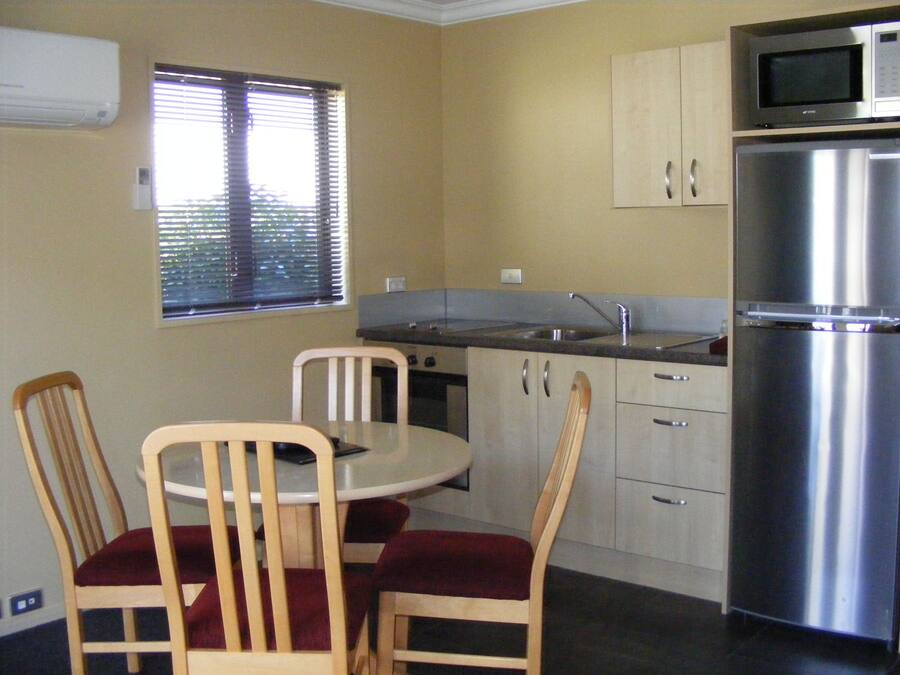 A compact kitchen with a dining table, chairs, a refrigerator, a microwave, and a window with blinds.