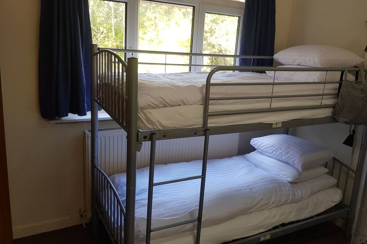 A bunk bed room with a window, curtains, and a wall-mounted lamp.