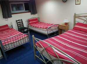 A room with two metal bunk beds, a single bed, a chair, a bedside table with a lamp, a window with curtains, and a radiator. - Alba Hostel Glasgow (Glasgow)
