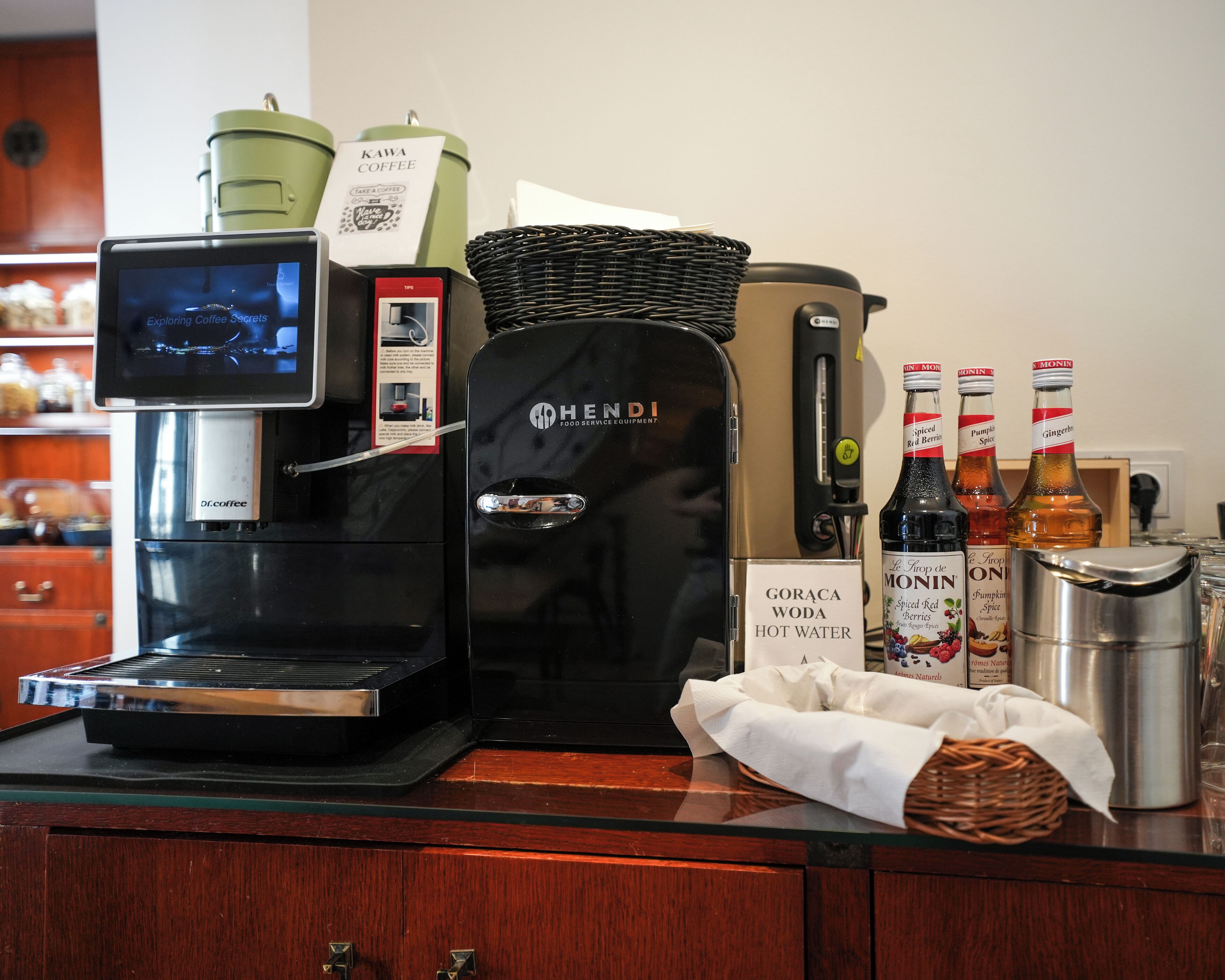 Een koffiehoek met een koffieapparaat, een heetwaterdispenser en flessen warm water.