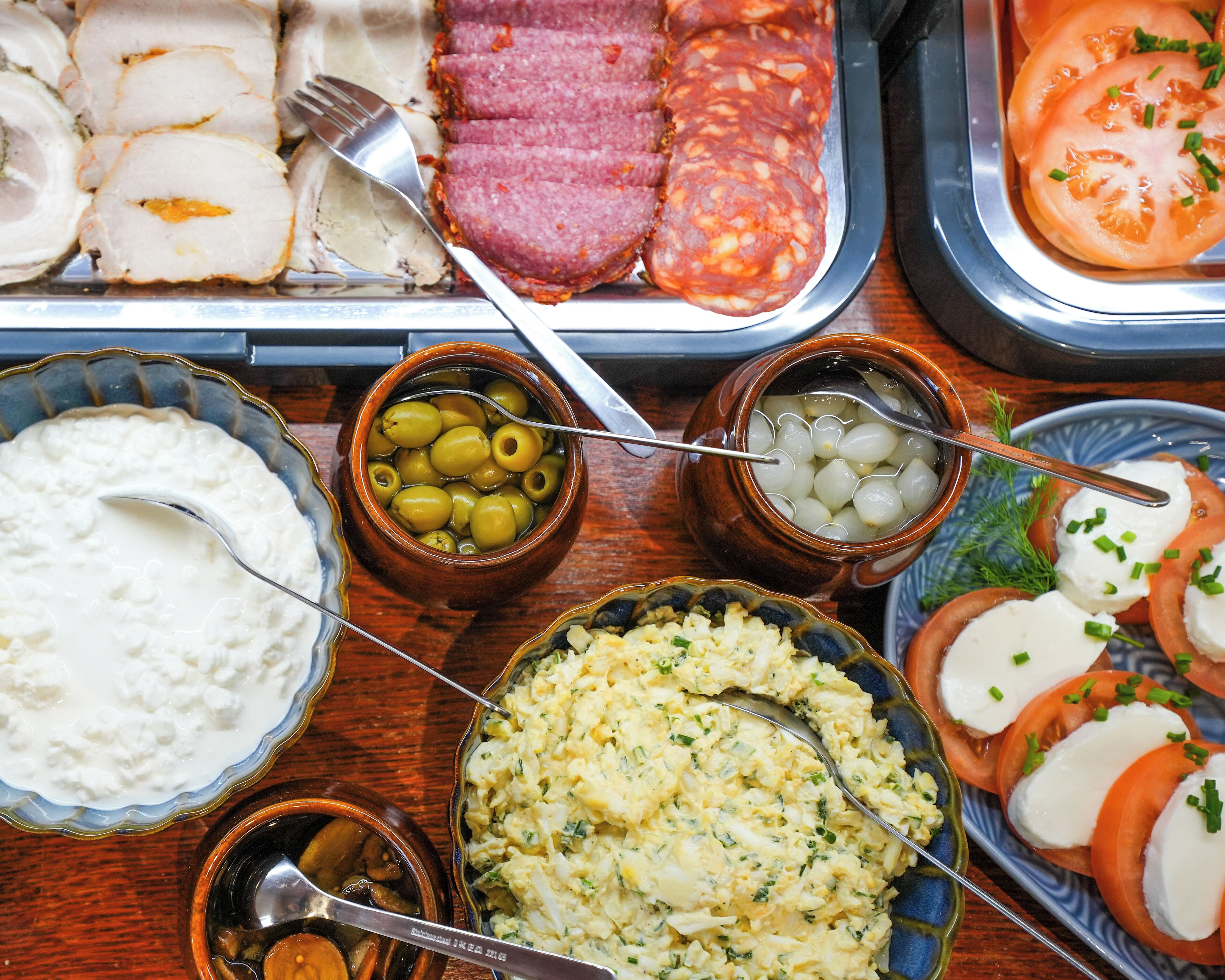 Diversos alimentos como embutidos, aceitunas y un tazón de queso fresco.
