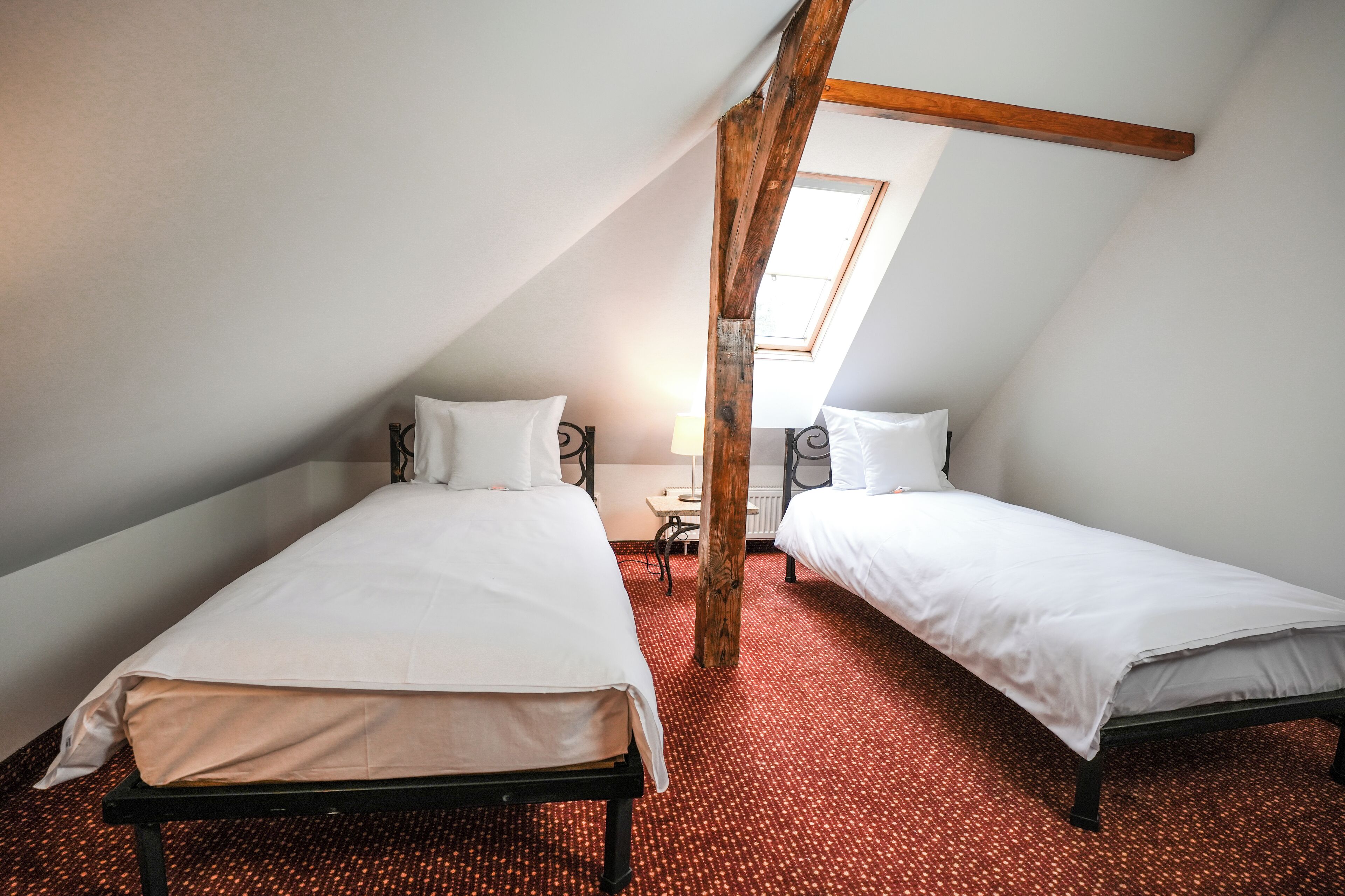 A bedroom with two beds, a wooden beam ceiling, and a red carpet.