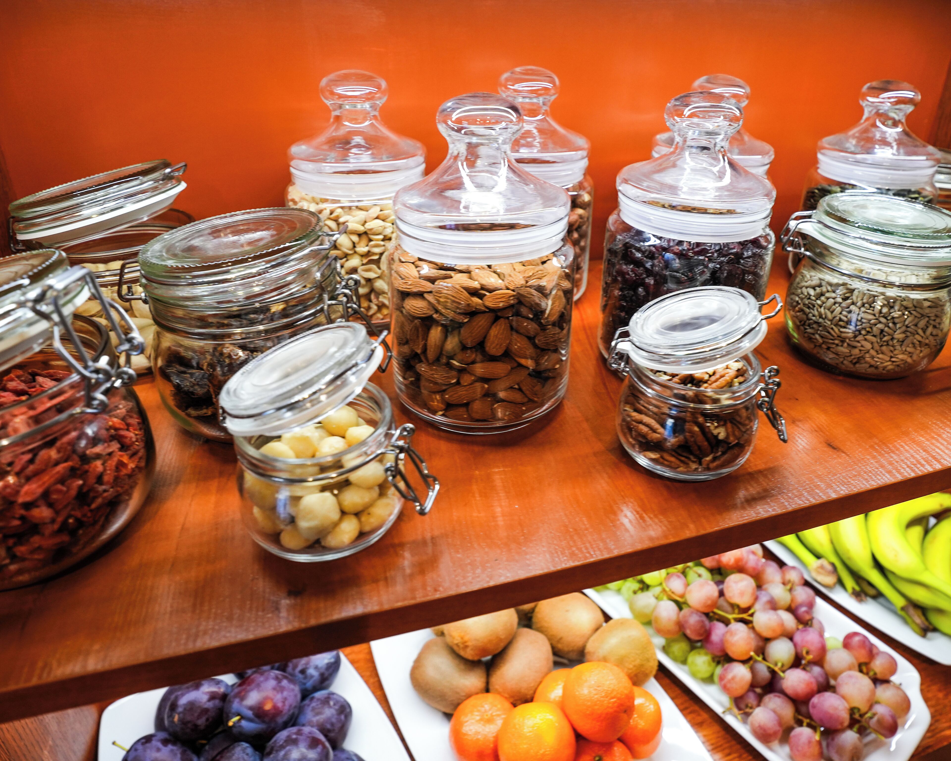A variety of food items in glass jars on a wooden table against an orange background.