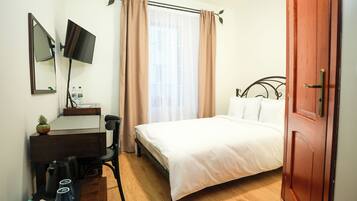 Un dormitorio con cama, escritorio con silla, televisor y ventana con cortinas.