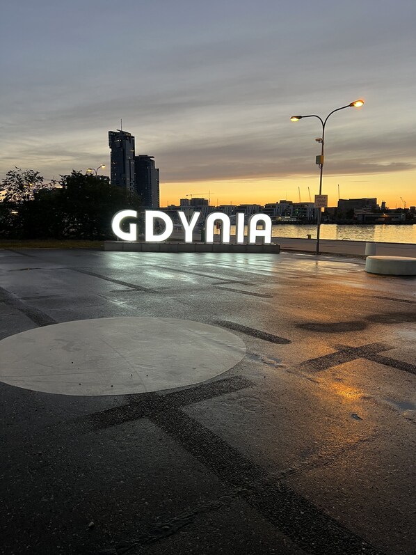 A wet pavement with a large illuminated sign reading "GDYNA" and a city skyline in the background. - Villa Admiral (Gdynia)