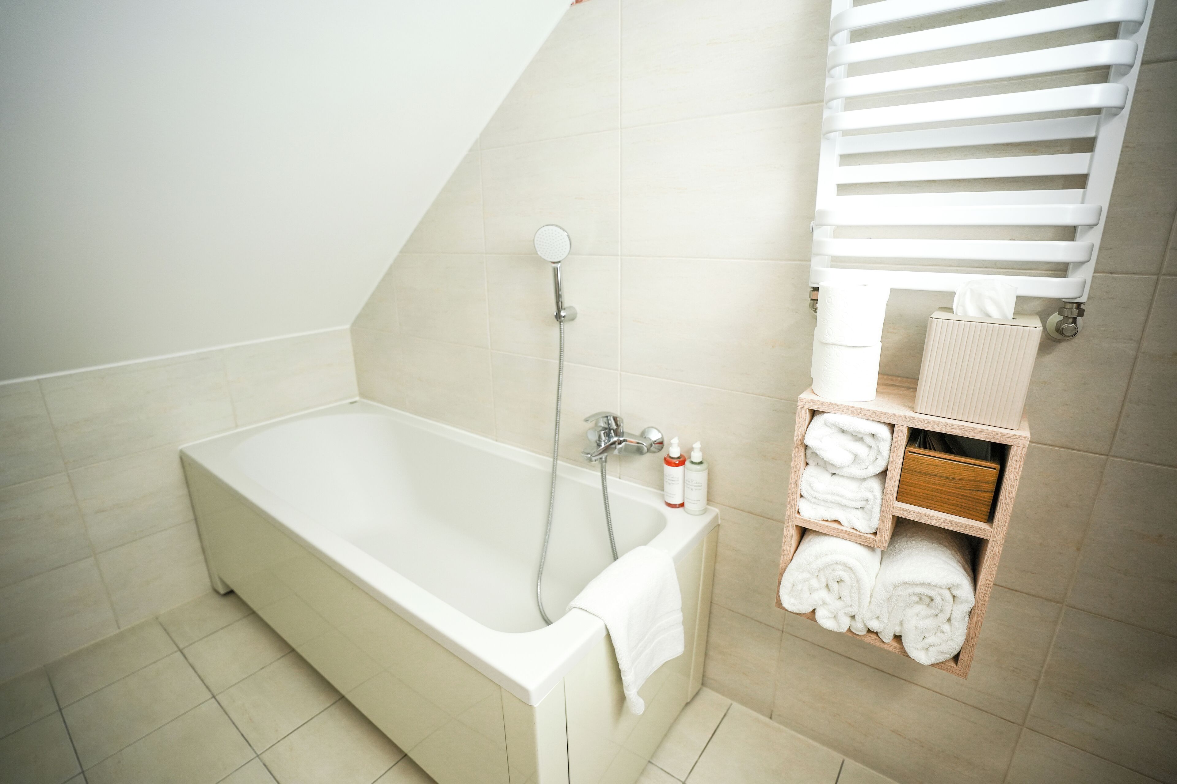A modern bathroom with a freestanding bathtub, a towel rack with folded towels, and a small wooden shelf with toiletries.