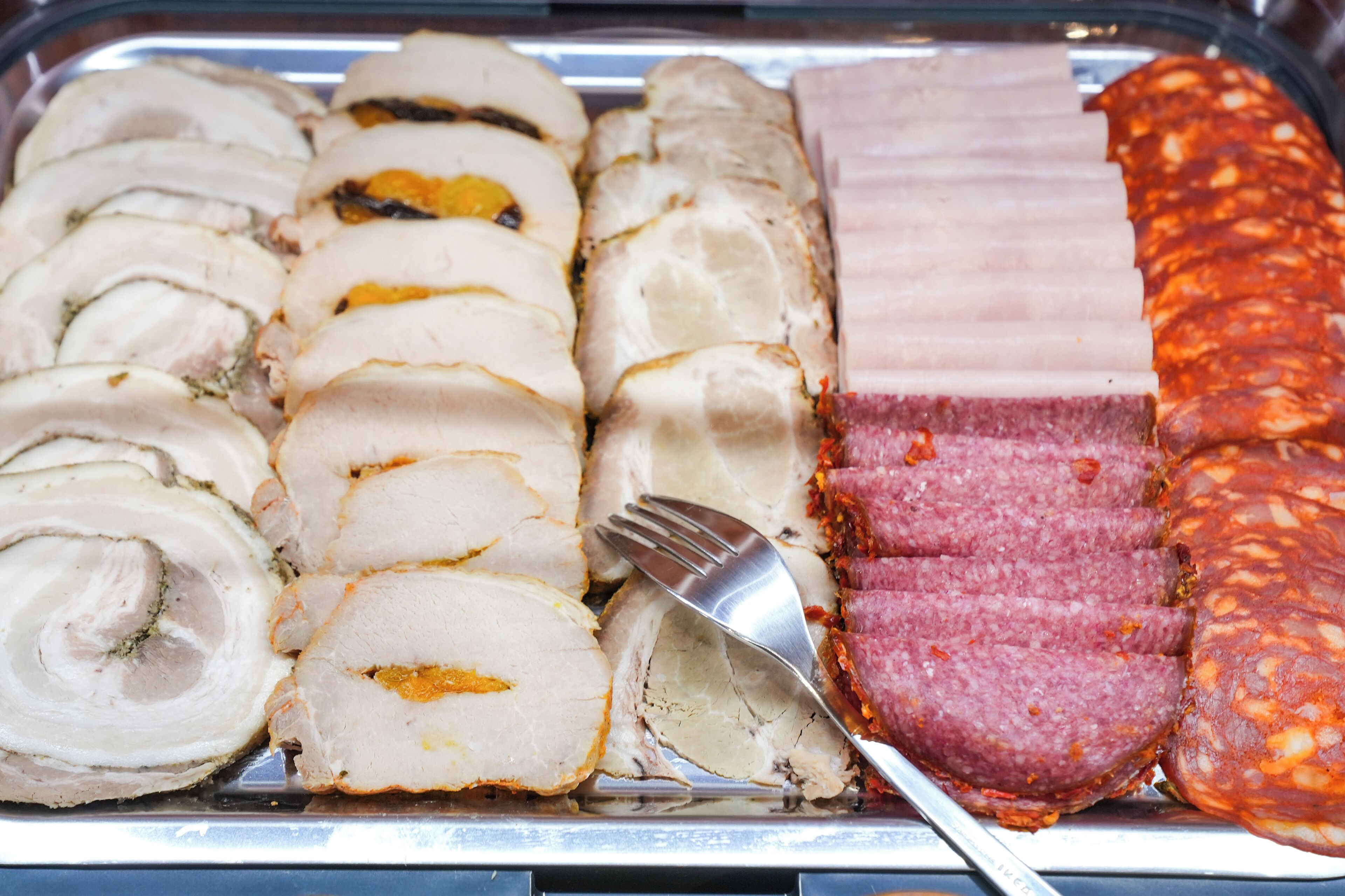 A variety of sliced meats including pork, ham, and salami on a tray.
