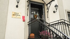 A building entrance with a sign reading "Villa Admirale 1929", a red emergency exit sign, and a staircase with wrought iron railings. - Villa Admiral (Gdynia)
