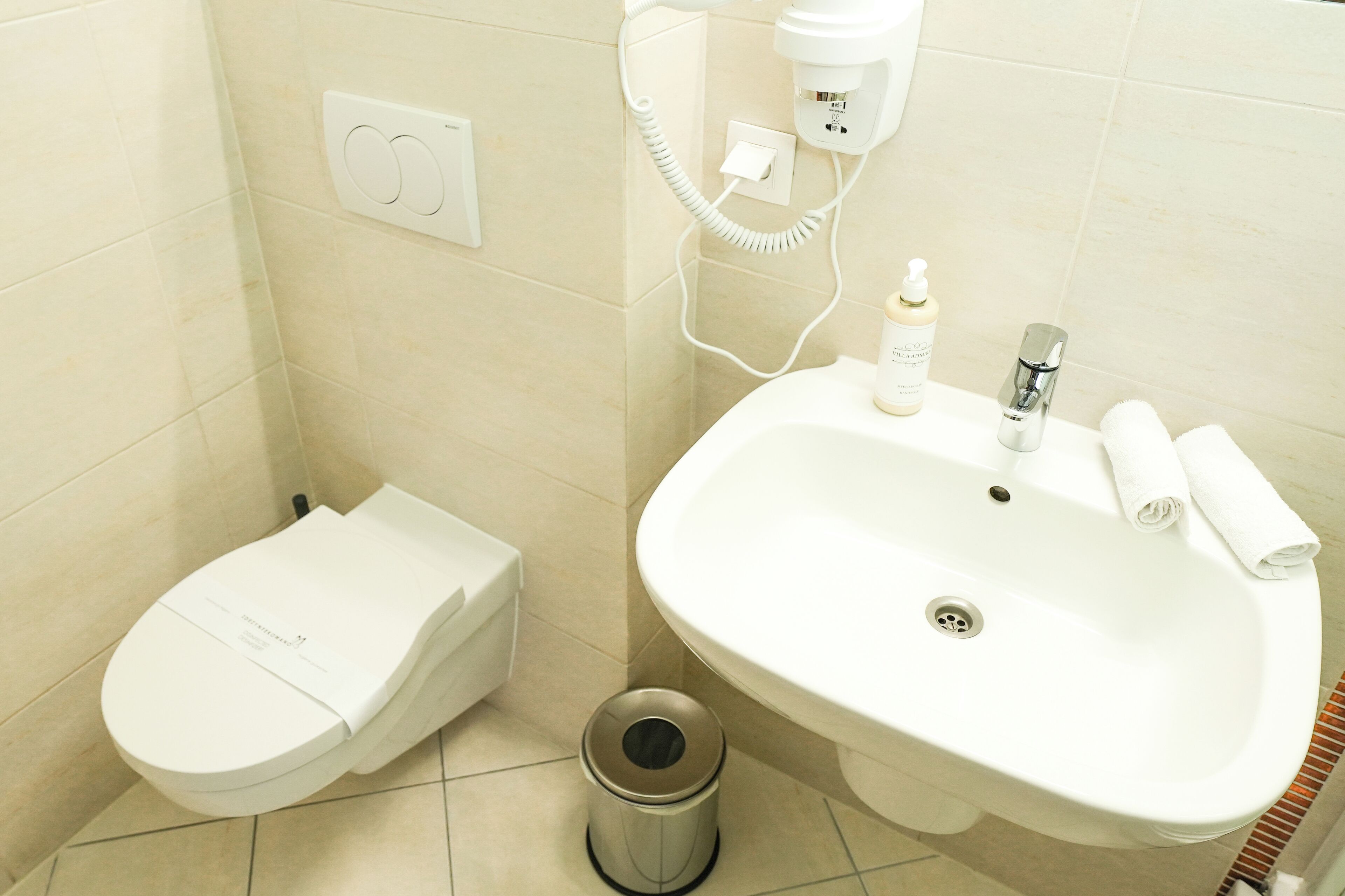 A bathroom with a toilet, sink, and a trash bin.