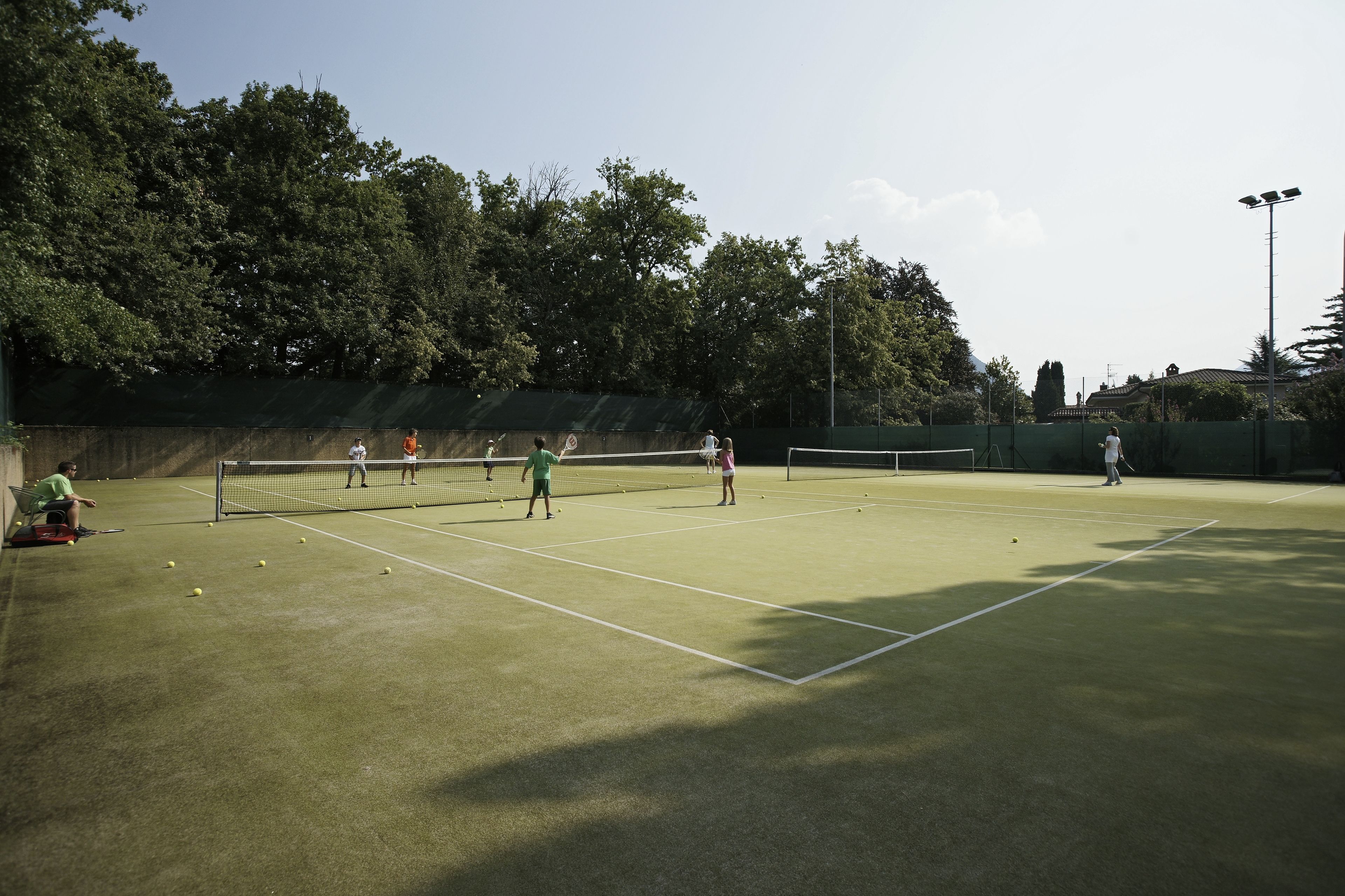 Un court de tennis en plein air, doté d’un filet, entouré d’arbres et délimité par une clôture.