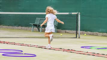 A tennis court with a net, a green wall, and a bench in the background.