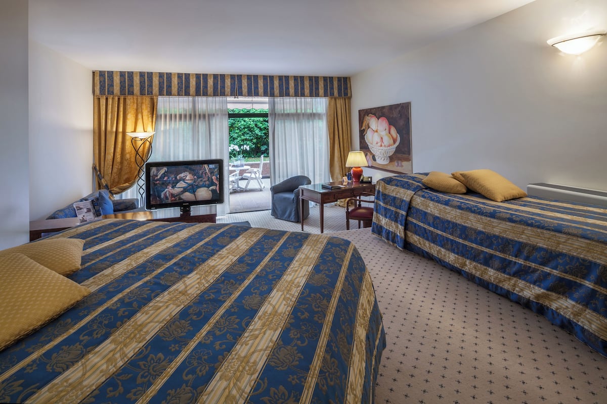 A hotel room with two beds, a desk, a chair, a television, and a painting.