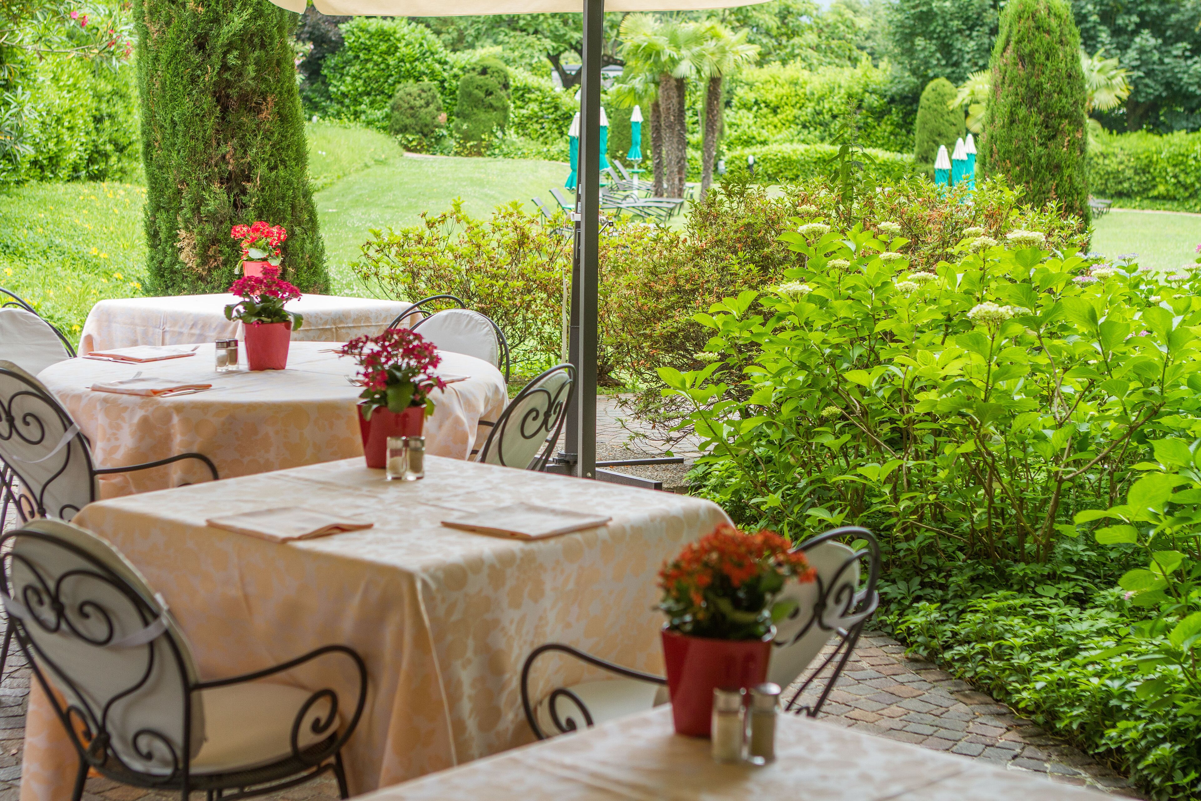 An outdoor dining area with tables and chairs, surrounded by lush greenery and a well-maintained garden.